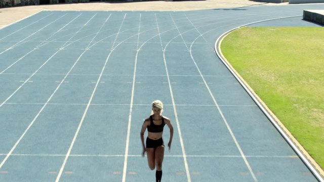 Fit woman running on racetrack during training session. Female runner practicing on athletics race track. Aerial moving shot.
