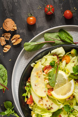 Salad. Spring vegetable salad. Fresh vegetable salad with tomatoes, apple, nuts, seeds and lemon. Olive oil pouring into bowl of salad.