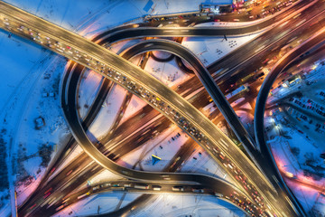 Aerial view of road in the modern city at night in winter. Top view of traffic in highway junction with illumination. Elevated road and interchange overpass. Busy intersection. Expressway and motorway