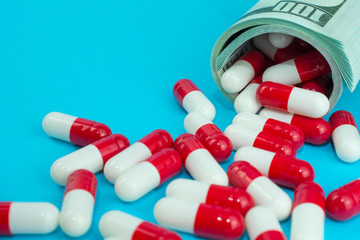 biotech and pharmaceutical companies. red white capsules spill out of folded dollars, blue background