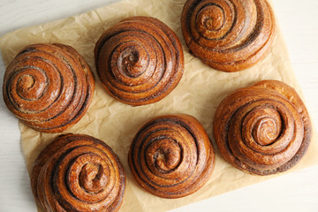 Parchment with cinnamon rolls on white wooden background, top view