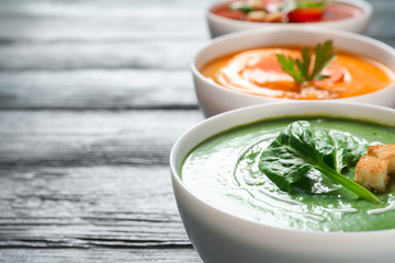 Various cream soups in bowls on wooden table. Space for text