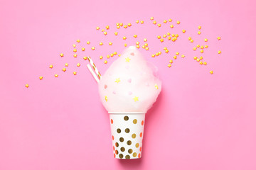 Cup with yummy cotton candy and sprinkles on color background, top view