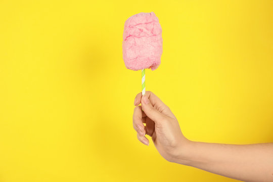 Woman holding straw with fluffy cotton candy on color background, closeup