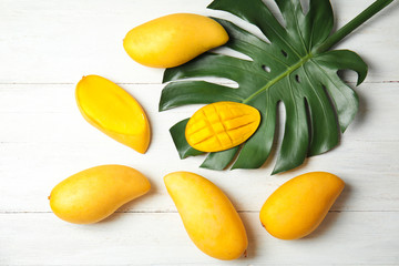 Flat lay composition with mango and tropical leaf on wooden background