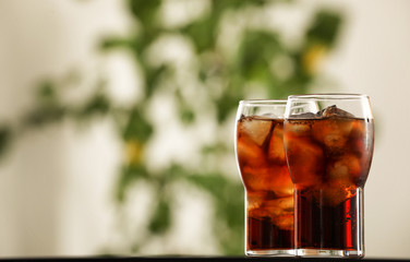 Glasses with cola and ice cubes on table against blurred background. Space for text