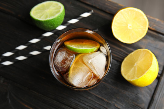 Glass of cocktail with cola, ice and cut lime on wooden table, flat lay