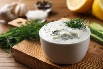 Fototapeta na wymiar Cucumber sauce with ingredients on wooden background, space for text. Traditional Tzatziki