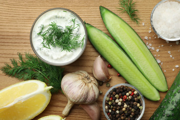 Tzatziki cucumber sauce with ingredients on wooden background, flat lay