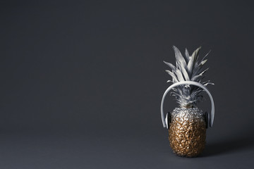 Pineapple with headphones on dark background. Space for text