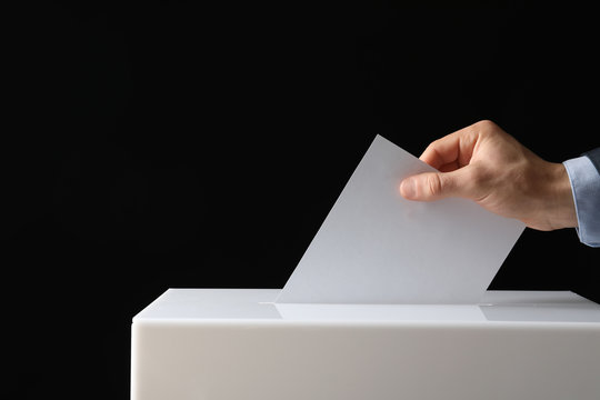 Man Putting His Vote Into Ballot Box On Black Background, Closeup