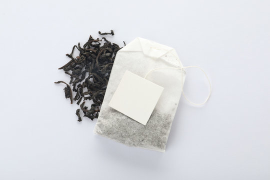 Dry tea leaves and unused bag with tag on white background, top view. Space for text