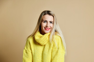 Beautiful blonde woman in yellow  sweater posing happy smiling on beige 