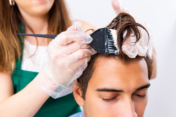 Woman hairdresser applying dye to man hair