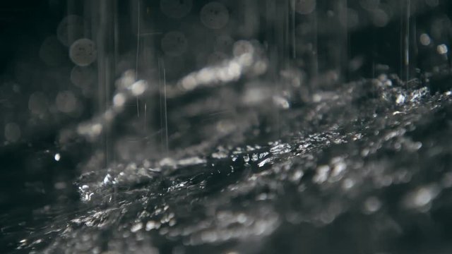 Beads of rainy water covering dark surface with shining spots in slow motion  