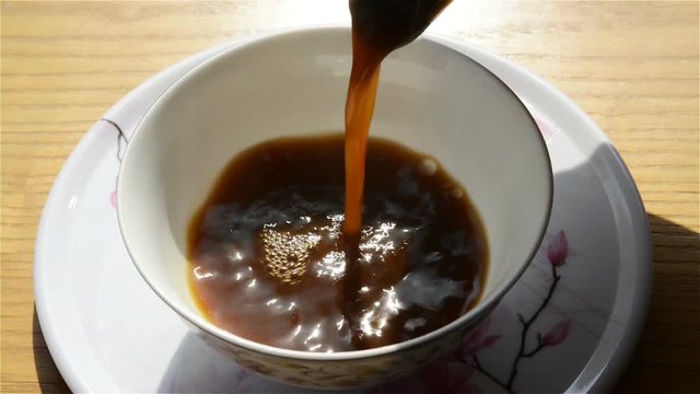 pouring herbal tea from an enamel pot with herb to a bowl