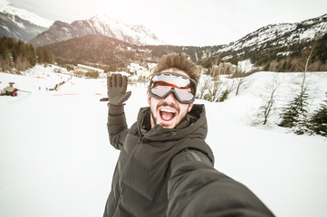 Fototapeta na wymiar Portrait of an andsome man is taking a selfie in the snow on a mountain at winter