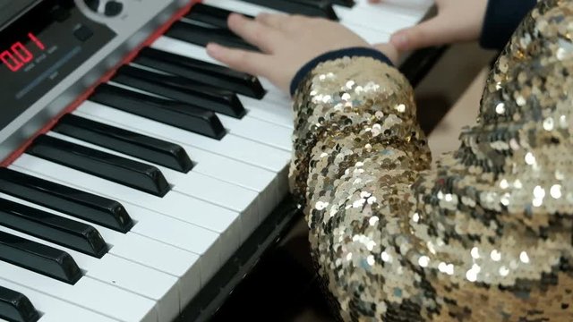 Teen girl in a shiny golden blouse plays the electric piano. Children's fingers press the keys of the synthesizer. Concert performance. Concept on the topic of musical youth.