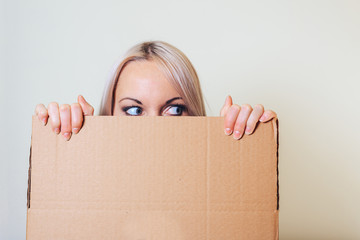 A young girl looks out of a cardboard box, with a frightened look.