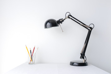 Retro black desk lamp and a glass of sharp pencil on white table top on white wall background with copy space product mock up placement