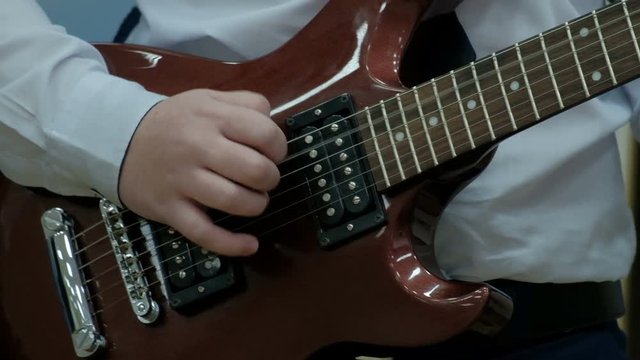 Close-up of the fingers of a teenager playing a brown electric guitar. The guy pulls the strings on a musical power tool. Concept musical theme of youth.