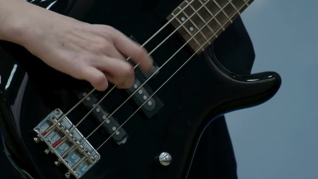 Close-up of the fingers of a teenager playing a black electric bass guitar. The guy pulled the strings on a musical power tools. Concept musical theme of youth.