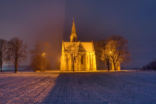 Nachtansicht der Kirche zwischen B&auml;umen auf einem schneebedeckten Feld