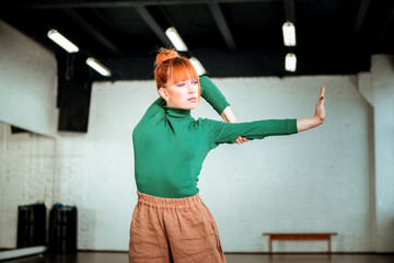 Pretty red haired girl in a green turtleneck standing in asana