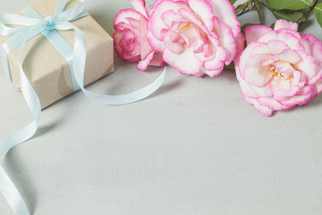 Gift or present box wrapped in kraft paper and pink rose flower on gray table