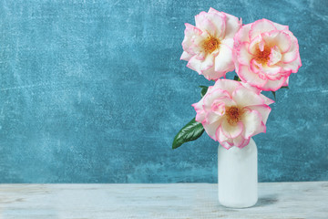 Roses in retro white vase on wood table on grunge blue wall with copy space.