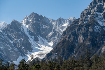 Jade dragon snow mountain situated in Yulong, Yunnan China.  The snow covered mountain with rocky peaks with trees in the foreground giving a dramatic view.