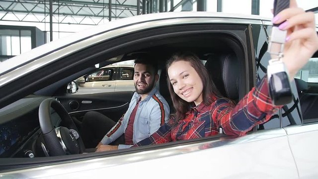 A young happy couple buys a new car. Smiles and shows the keys