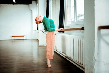 Red-haired professional ballet dancer with hair bun standing near ballet bar