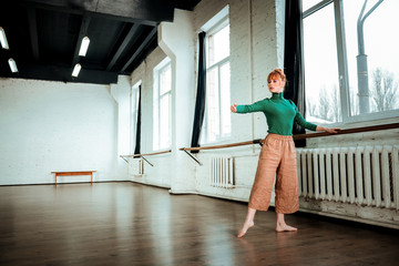 Young professional modern dancer with red hair training near ballet bar