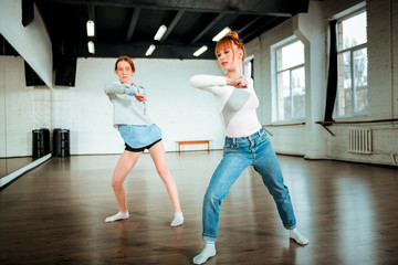 Fototapeta na wymiar Beautiful red-haired professional dancer in blue jeans and her student moving energetically