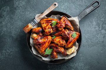 Baked chicken wings in barbecue sauce with sesame seeds and parsley in a cast iron pan on a dark...