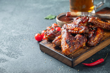 Roasted chicken wings in barbecue sauce with sesame seeds and parsley on a wooden board on a concrete table. With copy space. Tasty snack for beer on a dark background