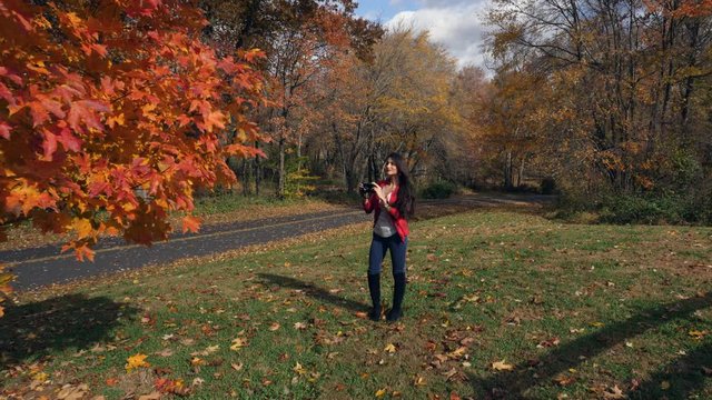 Beautiful young woman with retro camera in park photographing the fall colors