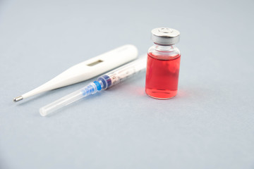 Medicine bottle for injection. Medical glass vials, thermometer and syringe for vaccination. Liquid red drug or vaccine for treatment, flu in laboratory, hospital, healthcare, or pharmacy
