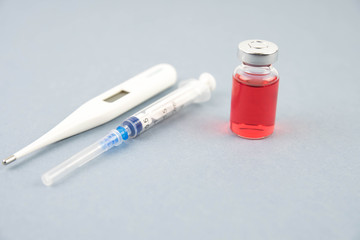 Medicine bottle for injection. Medical glass vials, thermometer and syringe for vaccination. Liquid red drug or vaccine for treatment, flu in laboratory, hospital, healthcare, or pharmacy