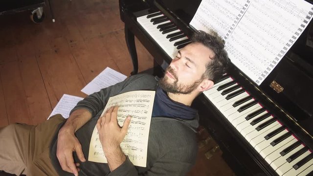 Male music composer sleep over an old piano holding music sheets. Dreaming with music