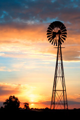 A silhouette of an old windmill on a farm against a beautiful sunset.