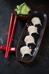 Plate with steamed dim sum dumplings over dark brown stone background, vertical shot