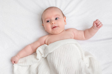 Newborn baby is lying on back on white blanket