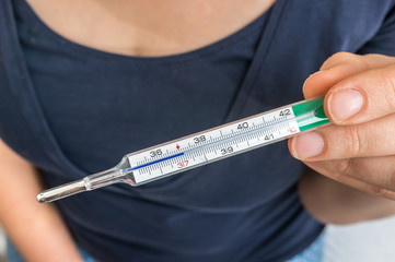 Woman with fever is holding mercury thermometer