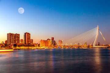 Erasmus-Brücke über die Maas mit Wolkenkratzern und Mond in Rotterdam, Südholland, Niederlande während der Dämmerung Sonnenuntergang. Rotterdam-Panorama