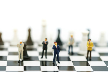 Miniature people: Businessman handshake to business success on chessboard. Commitment, agreement, investment and partnership concept