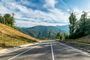 Naklejka premium Asphalt mountain road. Blue sky with white clouds.