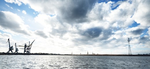 Distant view of port cranes and abandoned power line support over the surface of water