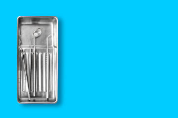 Dental instruments in a bowl. Dental mirror, probe hook, tweezers on blue background with free space. Dental hygiene and healthcare concept.